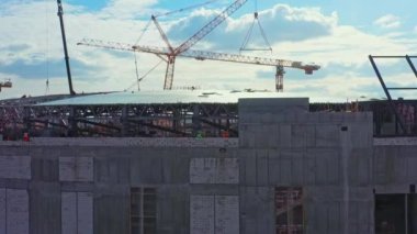 Future sports arena building with unfinished roof and tower cranes under cloudy sky aerial view. Construction site technology
