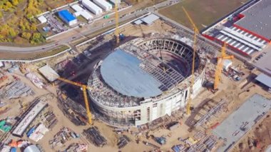 Half roofed sports arena building with high tower cranes near shopping mall in city bird eye view. Construction industry