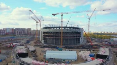 Sports center building with concrete carcass and cranes against apartment block aerial view. Construction site technology