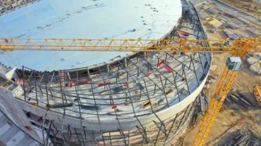 Unfinished sports center with carcass and tower cranes against residential district aerial view. Construction site
