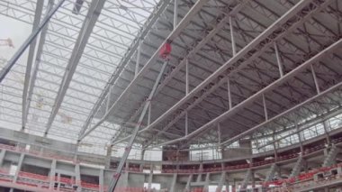 Roof carcass supported by crane hoists at sports stadium construction site low angle shot. Powerful machinery for building