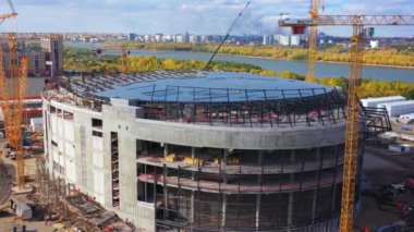 Future sports arena building and high tower cranes on riverbank in town aerial view. Contemporary construction site