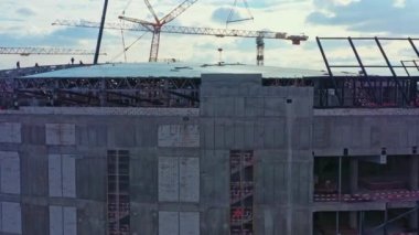 Unfinished stadium with concrete facade and partly covered roof against residential block bird eye view. Construction site