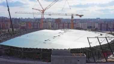 Sports stadium building roof assembling with tower cranes under cloudy sky aerial view. Construction site in city