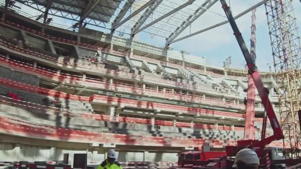 未完成のスポーツスタジアム建設現場で安全柵を持つ部族の近くの労働者やクレーン 建築業 — ストック動画