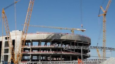 Timelapse of yellow cranes lifting huge roof carcass part at sports arena building construction site on sunny summer day