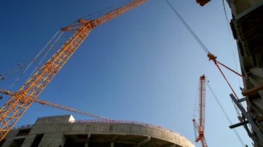 Timelapse of high yellow cranes lifting heavy detail at sports stadium construction site on sunny day low angle shot