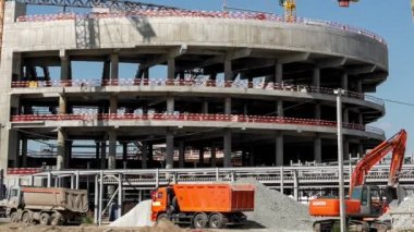 Timelapse of excavator loading building materials into tipper truck at sports arena building construction site on sunny day