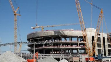 Timelapse of large metal frame detail installation on future sports arena roof with high cranes at construction site