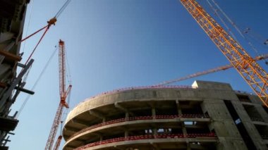 Timelapse of modern tower cranes operating with freights at sports stadium construction site on sunny day low angle shot