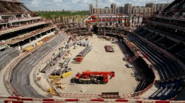 Timelapse of truck cranes driving along future sports arena at construction site on sunny summer day. Urban architecture