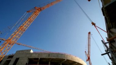 Timelapse of high tower cranes operating at new sports stadium construction site on sunny summer day low angle shot