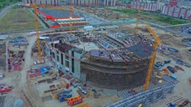 High yellow crane near unfinished sports stadium building at construction site in town bird eye view. Urban development