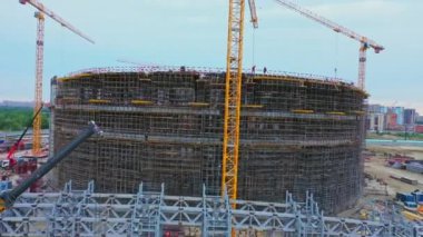 Large sports arena with builders and tower cranes at construction site in city district bird eye view. Building technology