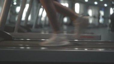 Woman in sneakers runs on contemporary treadmill training in sports gym close side view. Healthy lifestyle and activity