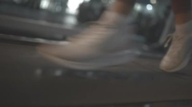 Athletic person in sneakers runs on modern treadmill training in gym close side view. Automatic equipment in sports club