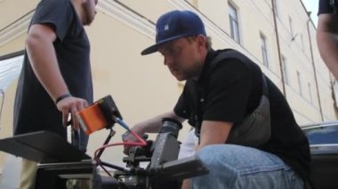 ALMATY, KAZAKHSTAN - JULY 20 2022: Cameraman wearing blue cap adjusts lens of professional camera for perfect angle. Staff prepares for shooting scene for film on July 20 in Almaty