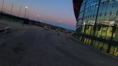 Empty yard of sports complex building with glass facade and streetlights in city on summer night first point view