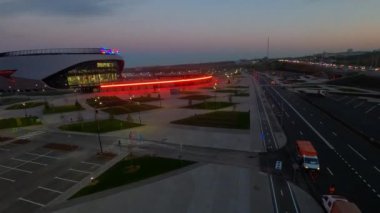 Bright red neon light on sports arena area in contemporary urban block in evening city first point view. Cityscape at dusk