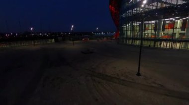 Spacious square near contemporary sports center with shining glass facade in night city first point view. Urban architecture