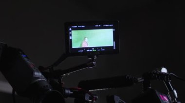 Small monitor on camera filming actor standing near green blackboard. Camera monitor for controlling process of film making at darkness
