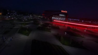 Large urban garden and athletic arena building with construction site machines in yard in night city first point view