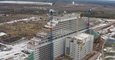 Modern yüksek katlı otel binası yapım aşamasında. Küçük bir kasabanın gelecekteki mimarisi ve kozalaklı orman hava manzarası.