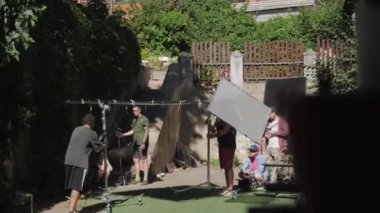 ALMATY, KAZAKHSTAN - JULY 14 2022: Filming crew adjusts light reflector for shooting scene on set. Staff prepares yard with equipment and supplies for filming on July 14 in Almaty