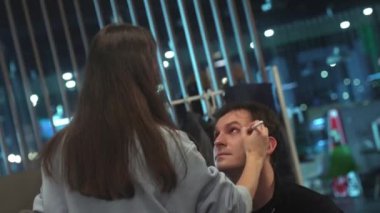 ALMATY, KAZAKHSTAN - JANUARY 27 2023: Female artist does makeup for professional actor on set. Woman prepares man for filming process using brush to paint face closeup on January 27 in Almaty