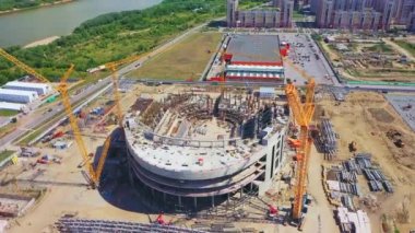 Nehir kenarındaki modern şehir stadyumunun inşaat sahasında. Büyük turnalar güneşli bir günde hava manzaralı turnuvalar için büyük spor sahaları inşa ederler.