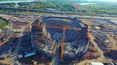 Gündoğumunda modern şehir arenası yapım aşamasında. Spor stadyumunun hava manzaralı inşaat sahasında büyük turnalar çalışıyor.