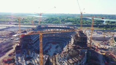 Güneşli bir sabahta stadyum inşaatında büyük sarı turnalar çalışır. Şehir havası görünümünde çağdaş arenanın inşa süreci