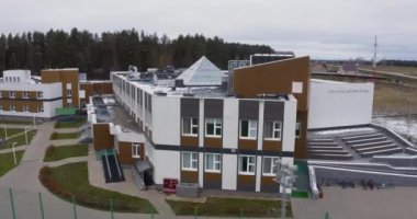 ALMATY, KAZAKHSTAN - OCTOBER 20 2022: Private school with small football stadium against grey sky aerial view. Grey and brown building surrounded by green trees on October 20 in Almaty