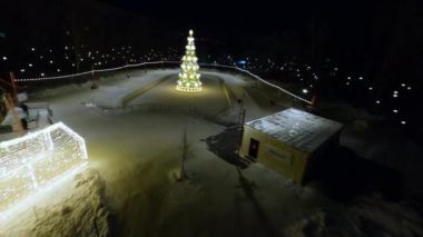 Snowy rink with delighted people skating around Christmas tree decorated with toys and garlands. Holiday spirit of New Year Eve