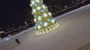 Snowy skating rink with decorated Christmas tree crowded with excited and amused people. Visitors enjoy Christmas holidays in park