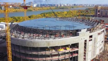 Big construction site with yellow building cranes and equipment. Huge roof on constructed football stadium bowl drone aerial view