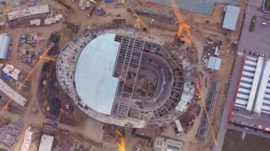 Big construction of new arena bowl on equipped building site with professional workers. Yellow building cranes for constructing arena