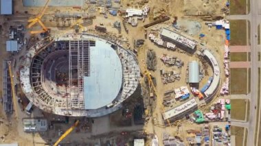 Construction of new stadium bowl at building site in well-established city. Building cranes for constructing new arena aerial view