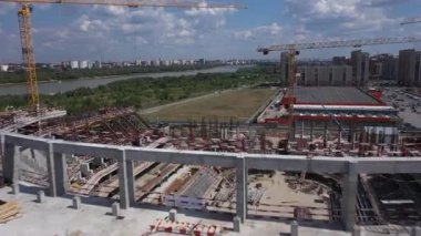 Process of building huge arena bowl for different events against big city. Tower cranes for constructing football stadium aerial view