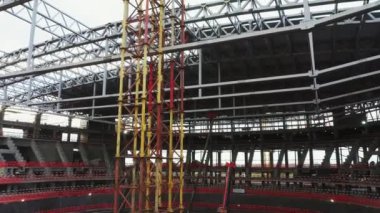 Yellow construction crane holding arena roof on building site. Process of constructing stadium bowl for football matches and concerts