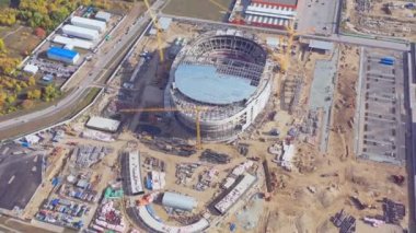 Process of constructing new football arena bowl at building site equipped with cranes. Construction of sports stadium aerial view