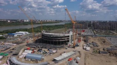 Construction cranes prepared for building of arena bowl. Building cranes constructing football stadium on riverbank near city aerial view