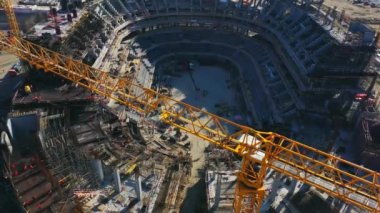 Yellow construction crane jib for building football arena in city. Team of professional workers prepares equipment for construction