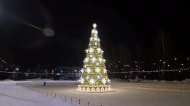 Girl skates about ice arena with decorated Christmas tree in night city aerial view. New year celebration in town