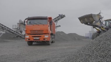 ALMATY, KAZAKHSTAN - 17 Şubat 2023: Kazıcı çakıl ocağında çalışan kamyon devrilmek üzere kova içinde yük taşır. Modern makineler 17 Şubat 'ta Almaty' de açık taş ocağında kaya cevheri çıkardılar.