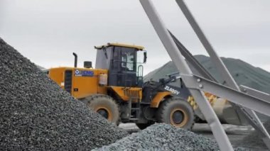 ALMATY, KAZAKHSTAN - 17 Şubat 2023: Kasvetli bir günde maden ocağında çakıl yığınları arasında sarı kazıcı sürücüler. 17 Şubat 'ta Almaty' de çukurda kovalı modern makine