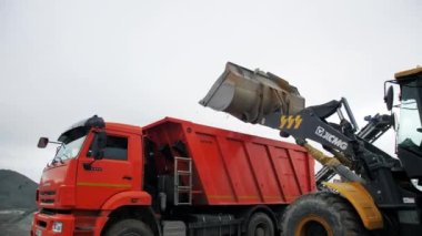ALMATY, KAZAKHSTAN - FEBRUARY 17 2023: Loading gravel into dump truck body with excavator bucket in mining pit on gloomy day. Machinery extracts ore at open quarry on February 17 in Almaty