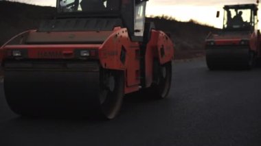 ALMATY, KAZAKHSTAN - 17 Şubat 2023: Çifte davulcular gün batımında otoyolda yeni asfalta basıyorlar. 17 Şubat 'ta Almaty' de kırsal kesimde yol çalışması makineleri