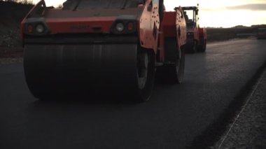 ALMATY, KAZAKHSTAN - FEBRUARY 17 2023: Worker drives double drum rollers along road lane with asphalt covering at sunset time. Maintenance process of modern highway on February 17 in Almaty