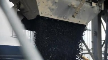 Hot mix asphalt poured down into tipper workbody from metal funnel at station closeup. Sustainable material used for road paving
